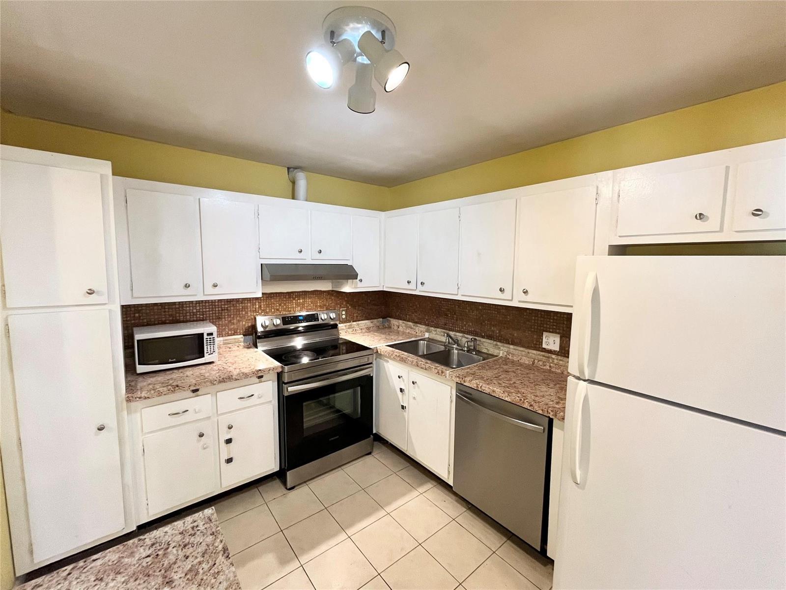 A kitchen features white cabinets, granite-look countertops, stainless steel appliances, and a brown tiled backsplash — 700 SE 2nd Avenue # 416, Deerfield Beach FL 33441, DEERFIELD BEACH, FL
