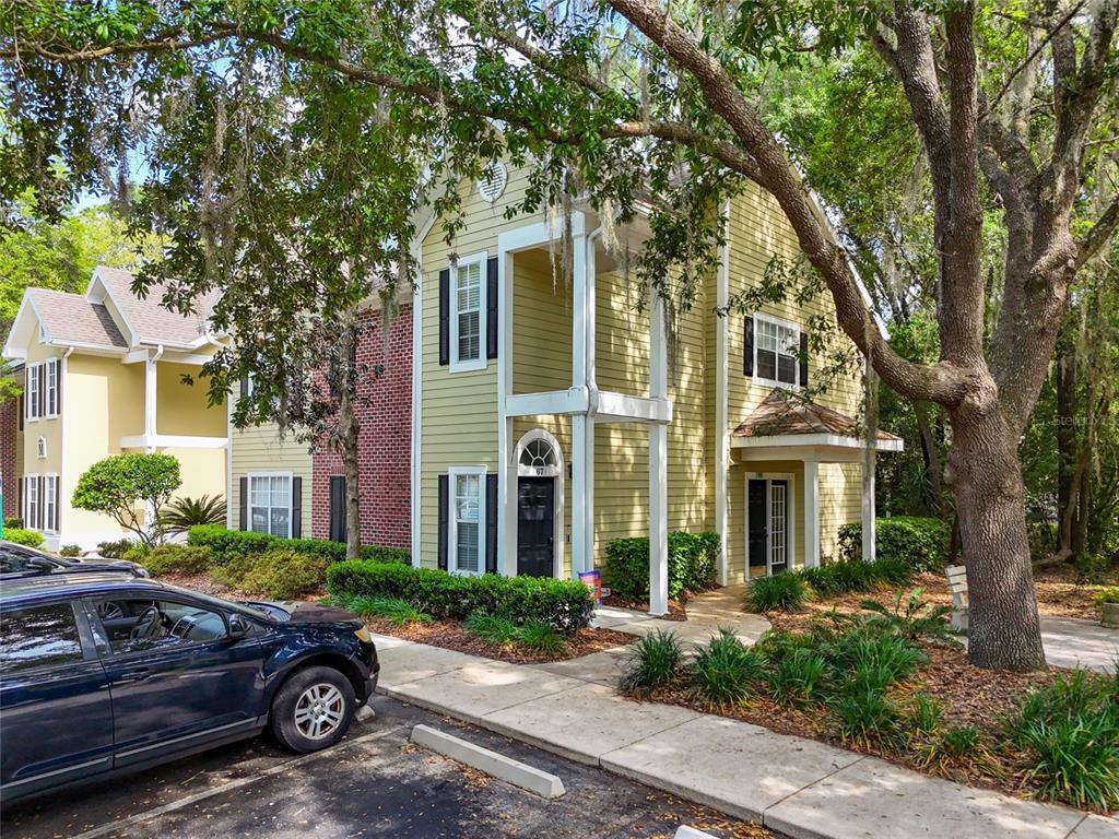 A two-story yellow building with black shutters and a brick accent wall near trees — 10000 SW 52ND AVENUE UNIT 68, GAINESVILLE, FL