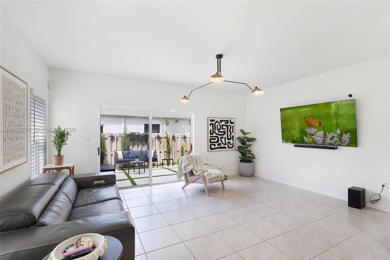 A living room features a grey leather sofa, a wall-mounted television, and a sliding glass door — 357 NE 1st Dr, Florida City FL 33034, FLORIDA CITY, FL