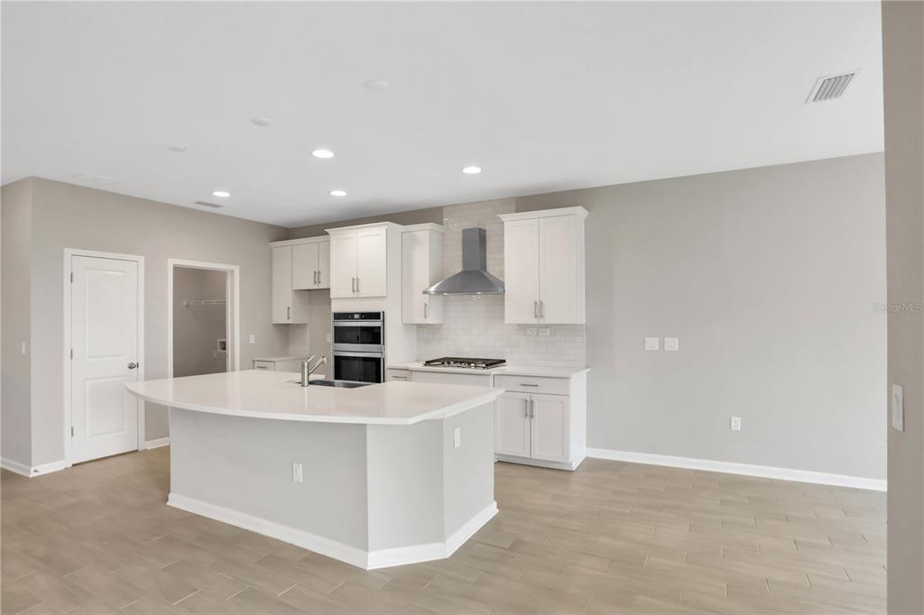 A modern kitchen features white cabinetry, a large island with a sink, and light flooring — 3852 HOLSTEIN WAY, GREEN COVE SPRINGS, FL