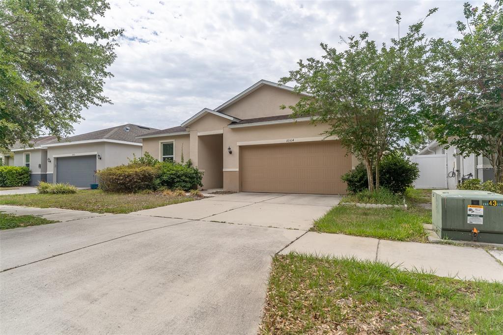 A single-story suburban house features a tan stucco exterior, a two-car garage, and a driveway — 10514 MEDFORD LAKE DRIVE, RIVERVIEW, FL