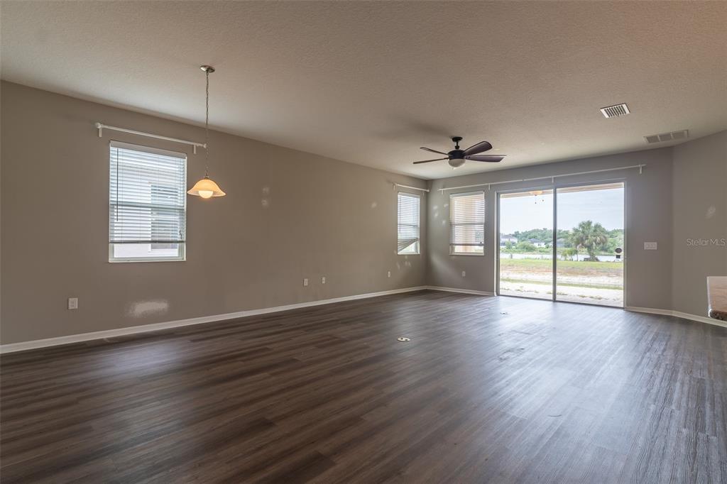 An empty living room features wood-look flooring, a ceiling fan, and sliding glass patio doors — 10514 MEDFORD LAKE DRIVE, RIVERVIEW, FL