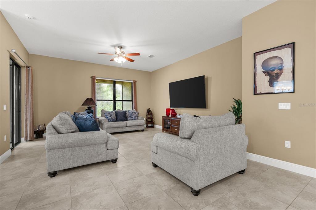A spacious living room with tile floors, a ceiling fan, and an open kitchen layout — 661 CARMEL LANE, POINCIANA, FL