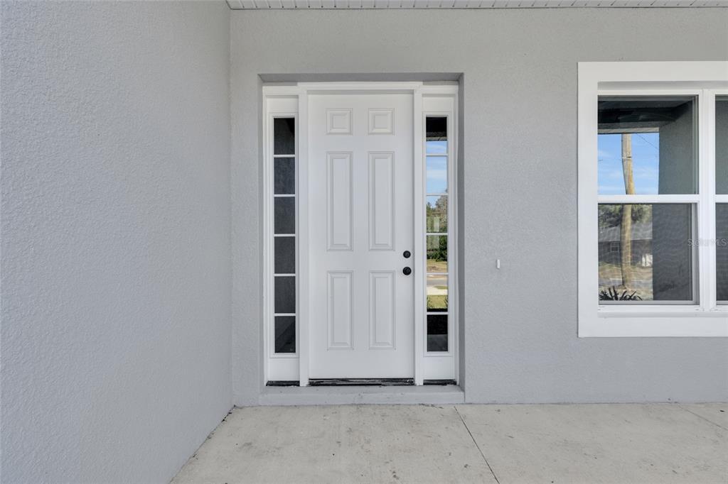 A white front door with side windows is set into a light gray exterior wall — 902 SW 2ND STREET, OCALA, FL