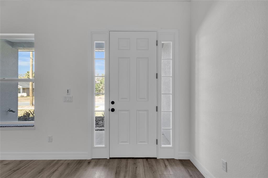 A white front door with sidelights and wood-look flooring in a bright, empty room — 902 SW 2ND STREET, OCALA, FL