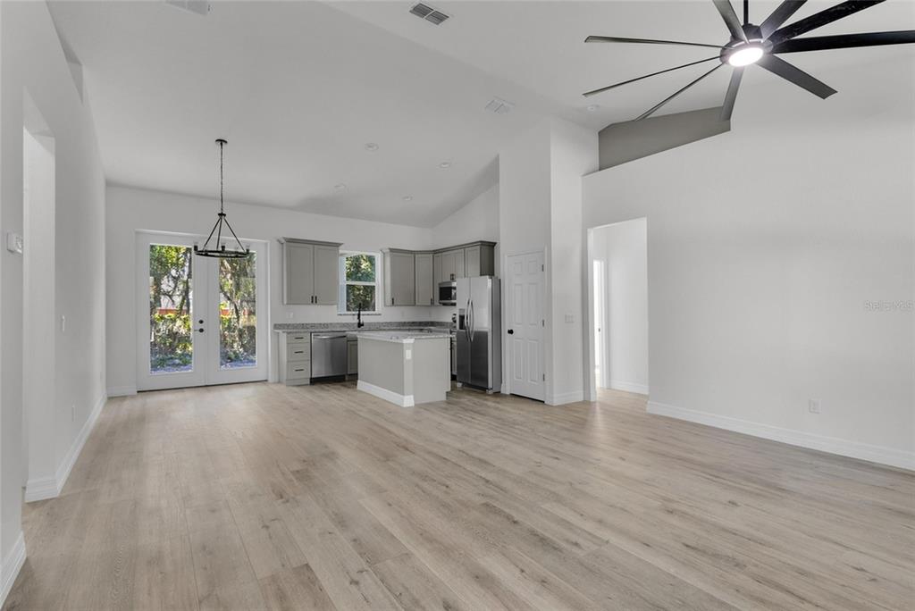 An open-concept kitchen and living area features light wood flooring, gray cabinets, and vaulted ceilings — 902 SW 2ND STREET, OCALA, FL