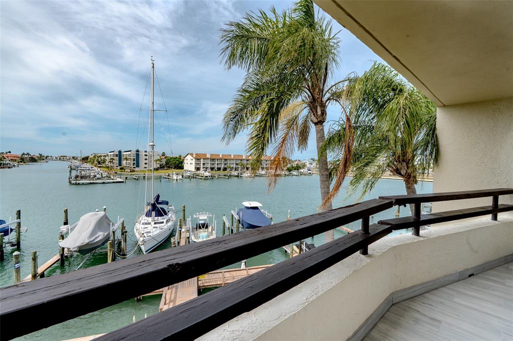 A balcony with a dark wooden railing overlooks a marina with boats and palm trees — 126 1ST STREET E UNIT 210, TIERRA VERDE, FL