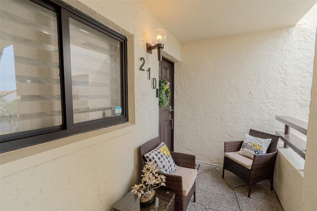 A covered balcony features two wicker chairs, a small table, and a brown entry door — 126 1ST STREET E UNIT 210, TIERRA VERDE, FL