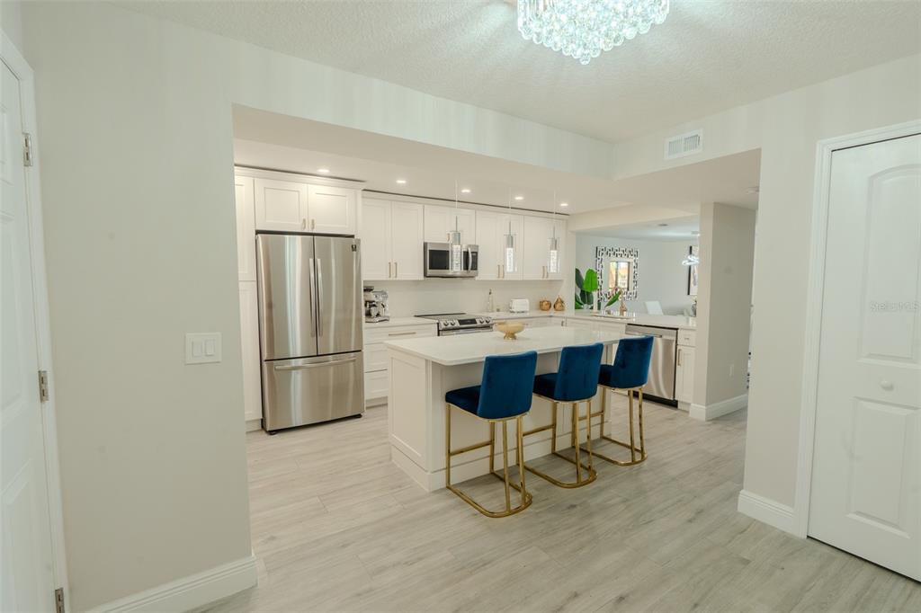 A modern white kitchen features a central island with three blue bar stools — 126 1ST STREET E UNIT 210, TIERRA VERDE, FL