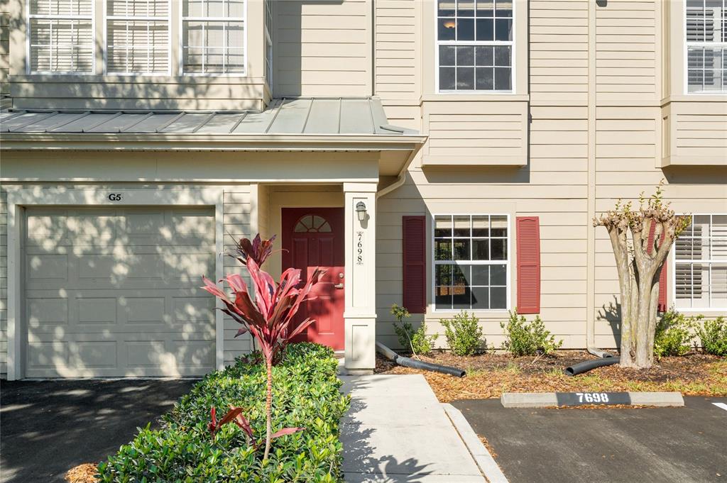 A tan two-story townhouse features a red front door, a garage, and a small garden — 7698 PLANTATION CIRCLE, BRADENTON, FL