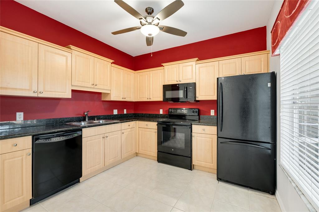 A kitchen features light wood cabinets, black appliances, dark countertops, and bright red walls — 7698 PLANTATION CIRCLE, BRADENTON, FL