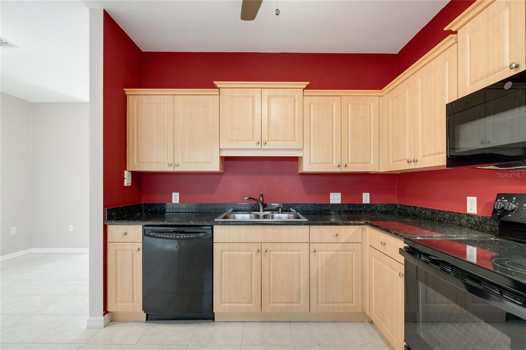 A kitchen features light wood cabinets, dark granite countertops, red walls, and black appliances — 7698 PLANTATION CIRCLE, BRADENTON, FL
