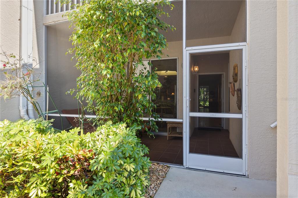 A screened-in patio features a large potted tree, tiled flooring, and a white screen door — 9611 CASTLE POINT DRIVE UNIT 915, SARASOTA, FL