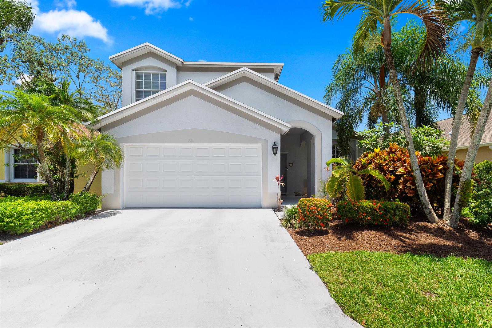 A two-story suburban house with a white garage, a concrete driveway, and tropical landscaping — 2211 Soundings Court, FL 33413, FL