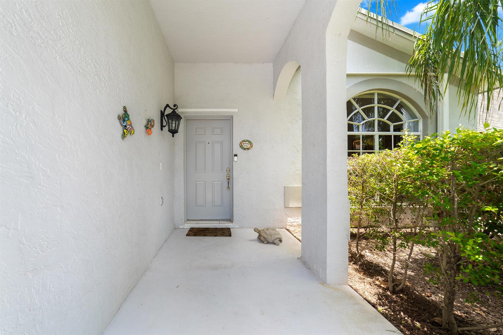 A covered entryway features a light gray front door, a turtle statue, and arched architecture — 2211 Soundings Court, FL 33413, FL