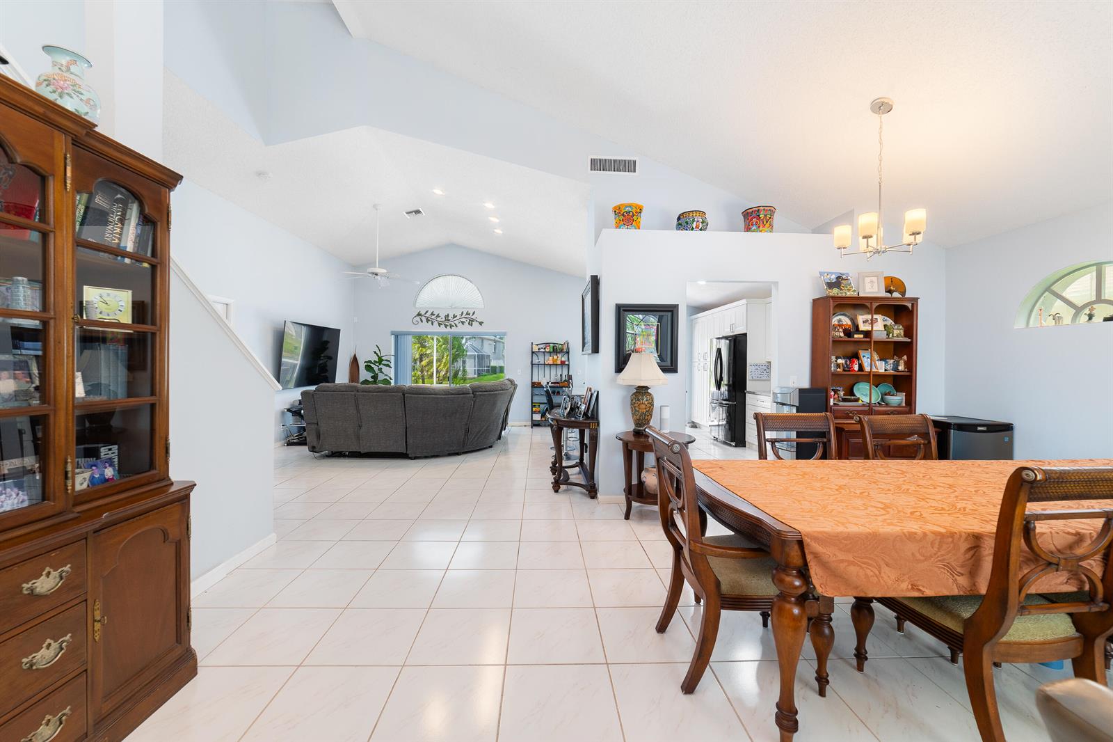 An open-concept living and dining area features vaulted ceilings, tile flooring, and traditional wood furniture — 2211 Soundings Court, FL 33413, FL