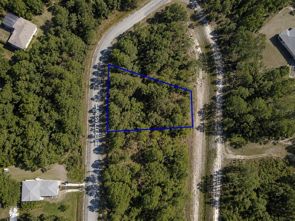 An aerial view shows a wooded, trapezoidal plot of land outlined in blue along a road — 2699 GAINESVILLE ROAD SE, PALM BAY, FL