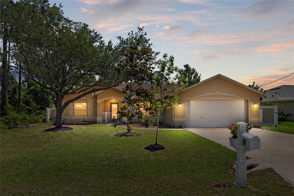 A single-story house with a two-car garage, a front lawn, and a large shade tree — 90 UNIVERSIAL TRAIL, PALM COAST, FL