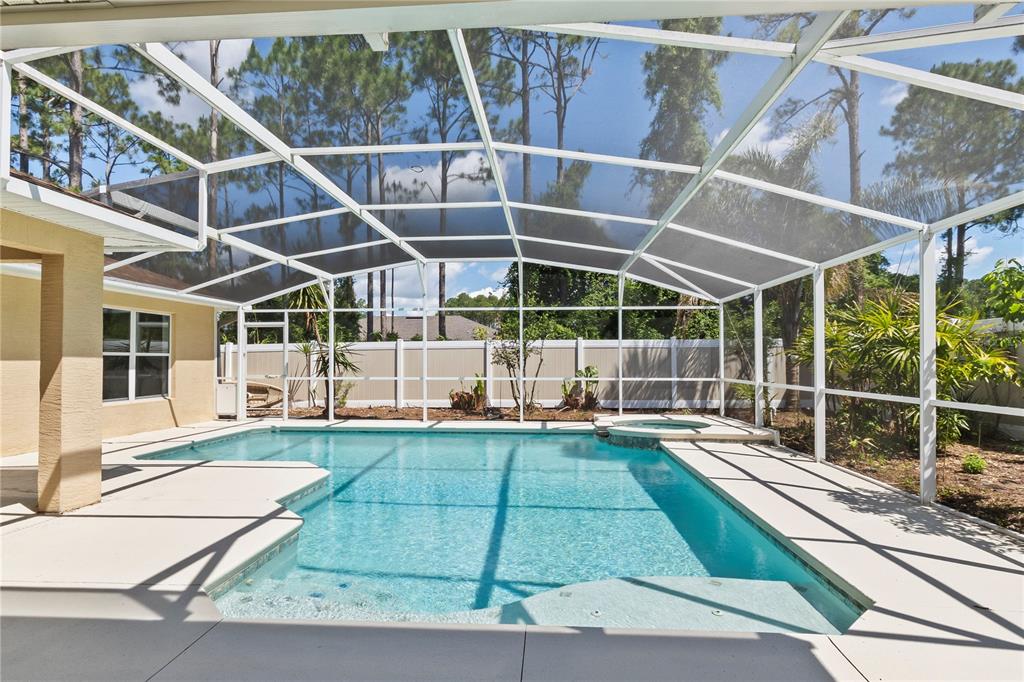 A screened-in swimming pool and hot tub sit on a patio behind a residential home — 90 UNIVERSIAL TRAIL, PALM COAST, FL