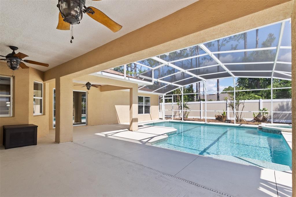 A covered patio with ceiling fans overlooks a screened-in swimming pool and backyard — 90 UNIVERSIAL TRAIL, PALM COAST, FL