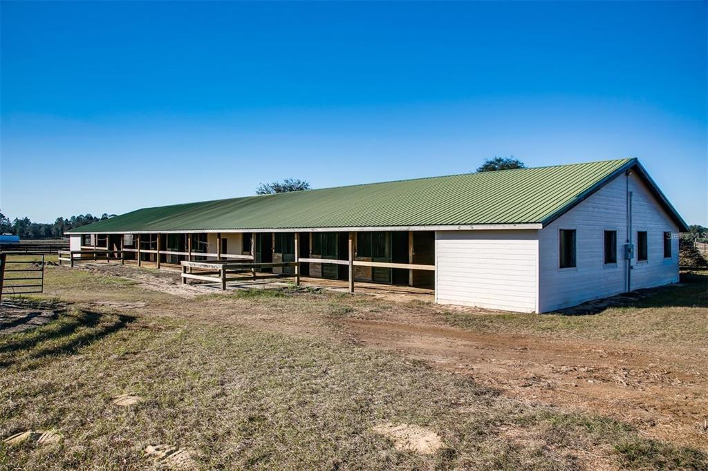 A long, single-story horse stable with a green metal roof and white siding — 2351 NE 120 AVENUE, WILLISTON, FL