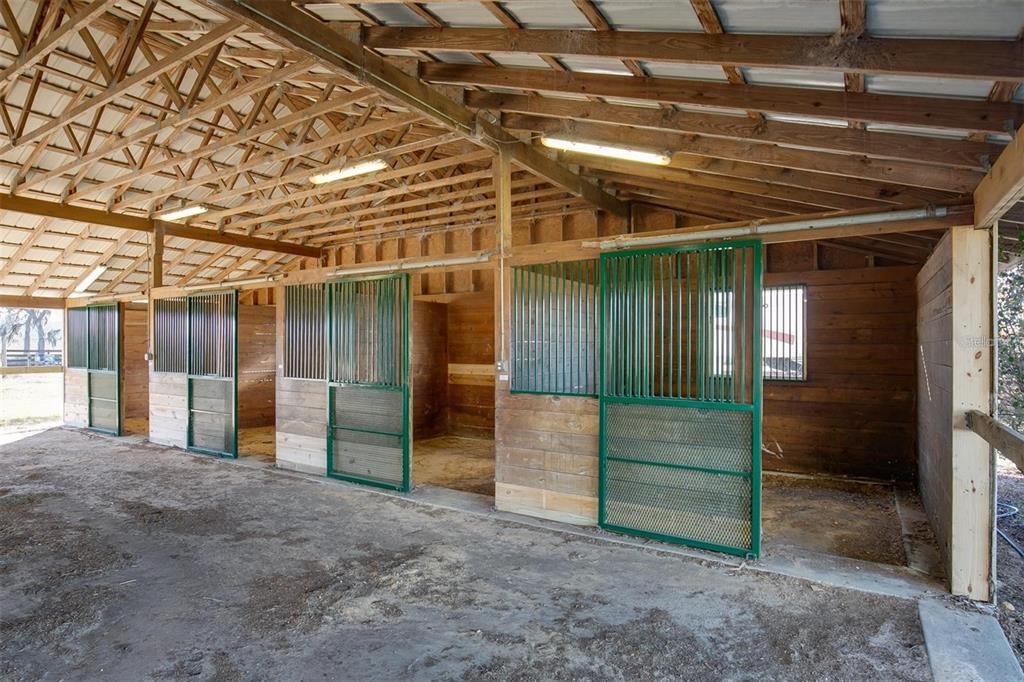 A row of horse stalls with green metal gates inside a wooden barn structure — 2351 NE 120 AVENUE, WILLISTON, FL