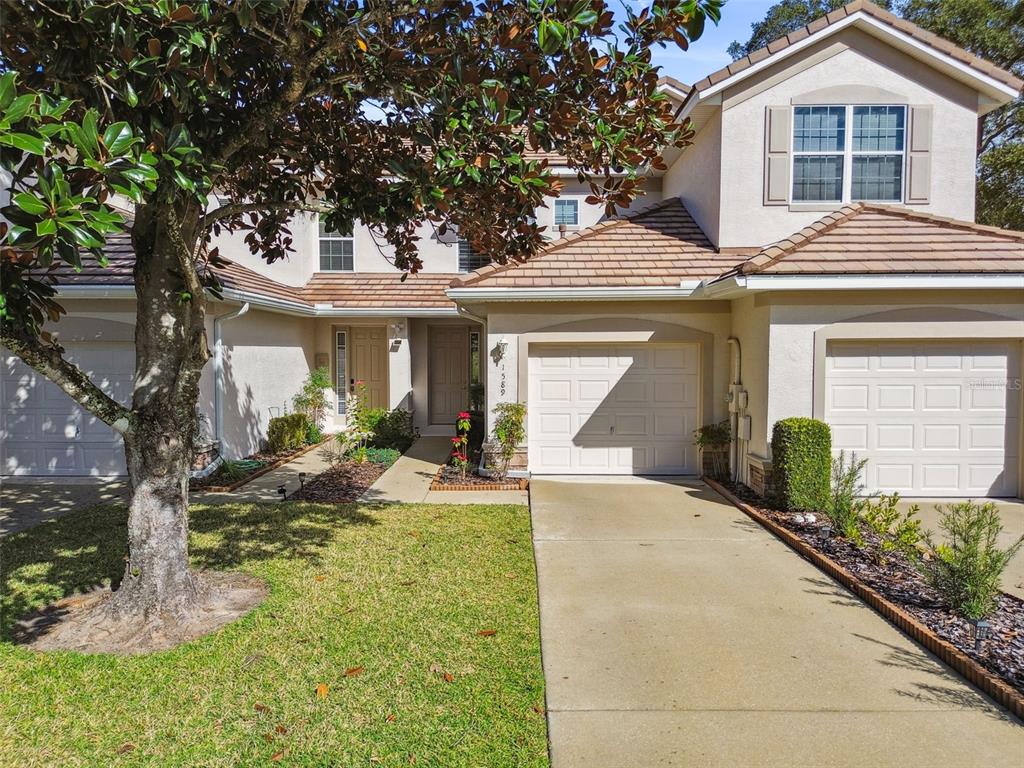 A two-story townhouse with a beige stucco exterior, two garage doors, and a front lawn — 1589 W SWEET OAKS COURT, LECANTO, FL
