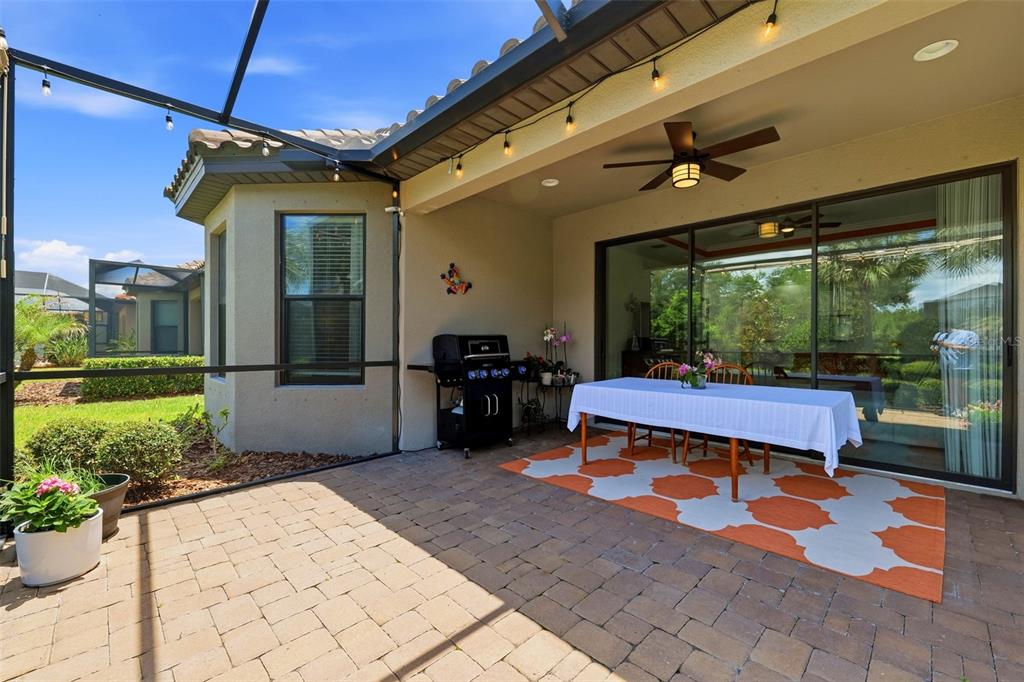 A covered brick patio features a dining table, a grill, and a ceiling fan — 8412 ALBERATA VISTA DRIVE, TAMPA, FL