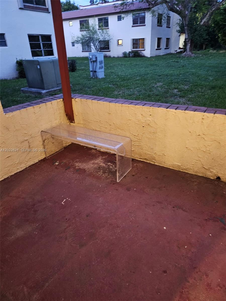 A concrete patio features a yellow stucco wall, a red floor, and a clear bench — 8650 SW 149th Ave # 305, Miami FL 33193, MIAMI, FL