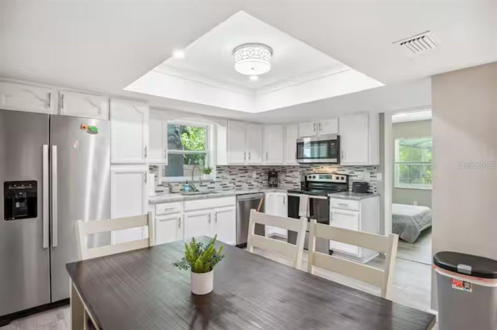 A kitchen with white cabinets, stainless steel appliances, and a dining table in the foreground — 6506 SEAFAIRER DRIVE, TAMPA, FL