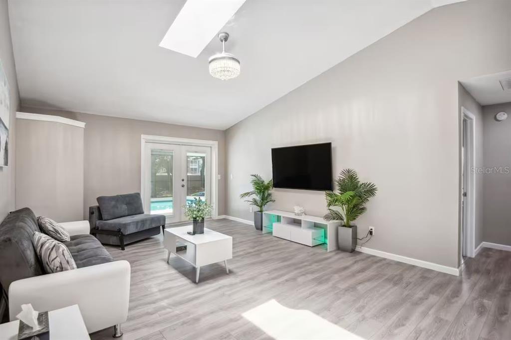 A living room with gray flooring, a wall-mounted television, and glass doors leading to a pool — 6506 SEAFAIRER DRIVE, TAMPA, FL