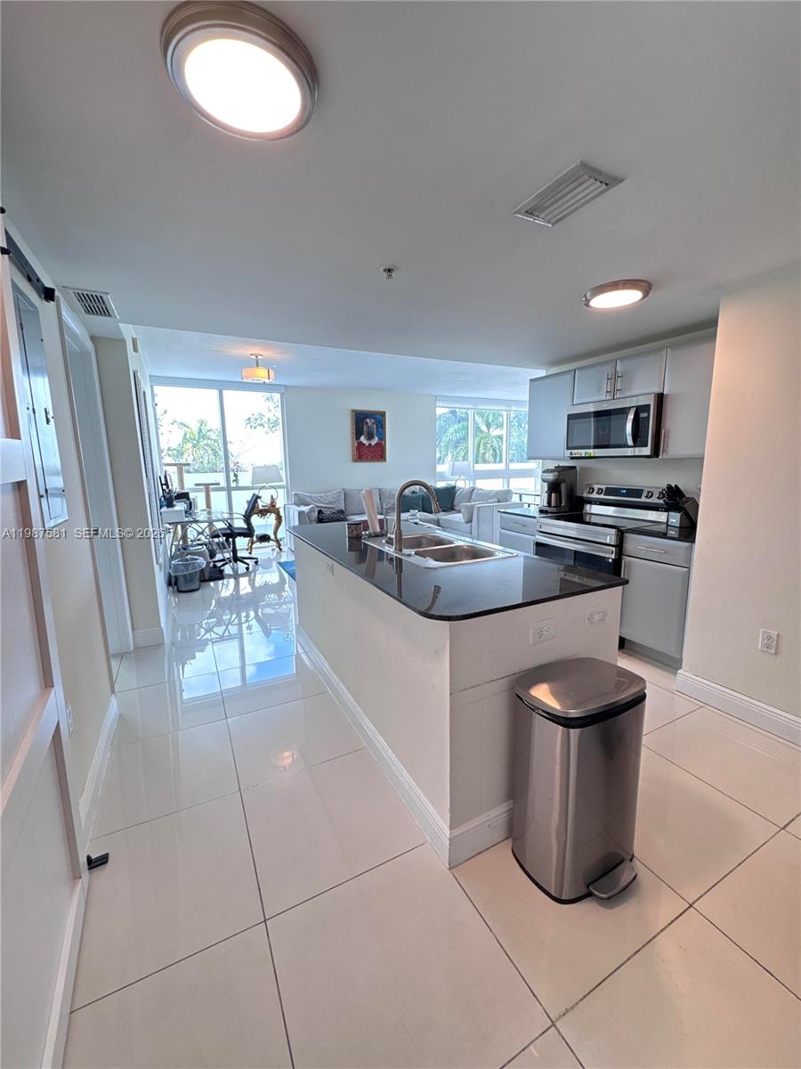 A kitchen with a dark island countertop and stainless steel appliances opens to a living area — 1861 NW S River Dr # 705, Miami FL 33125, MIAMI, FL