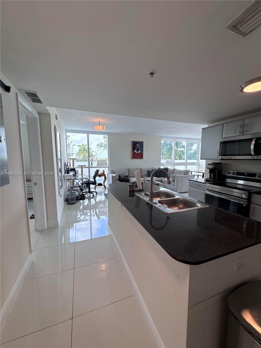 A kitchen with a black granite island and sink overlooks a living room with tile floors — 1861 NW S River Dr # 705, Miami FL 33125, MIAMI, FL