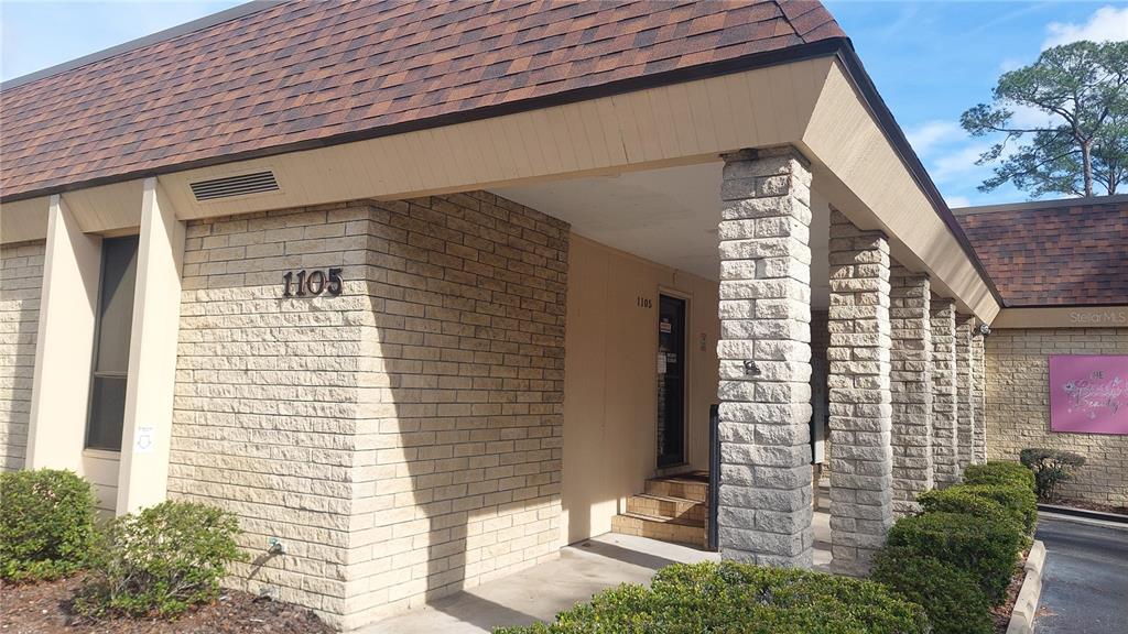 A brick commercial building exterior features a covered entrance with stone pillars and landscaping — 1103 NW 13TH STREET, GAINESVILLE, FL