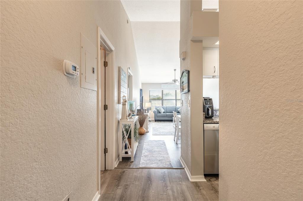 A hallway with wood-look flooring leads toward a living room and kitchen area — 402 BOUCHELLE DRIVE UNIT 204, NEW SMYRNA BEACH, FL