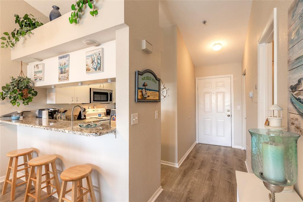 A kitchen with a granite breakfast bar and stools opens to a hallway with wood flooring — 402 BOUCHELLE DRIVE UNIT 204, NEW SMYRNA BEACH, FL