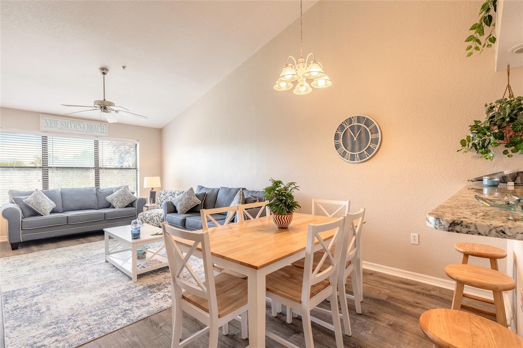 A living and dining area features a vaulted ceiling, gray sofa, and wooden dining table — 402 BOUCHELLE DRIVE UNIT 204, NEW SMYRNA BEACH, FL