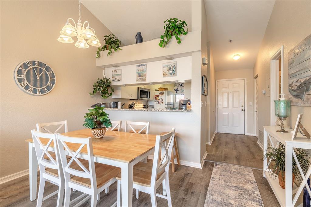 A dining area with a wooden table, white chairs, and an open kitchen pass-through window — 402 BOUCHELLE DRIVE UNIT 204, NEW SMYRNA BEACH, FL