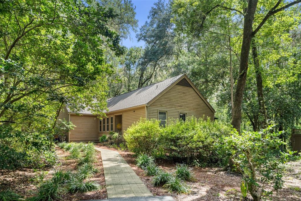 A tan, single-story house with horizontal siding is nestled in a wooded, landscaped yard — 5225 SW 86TH TERRACE, GAINESVILLE, FL