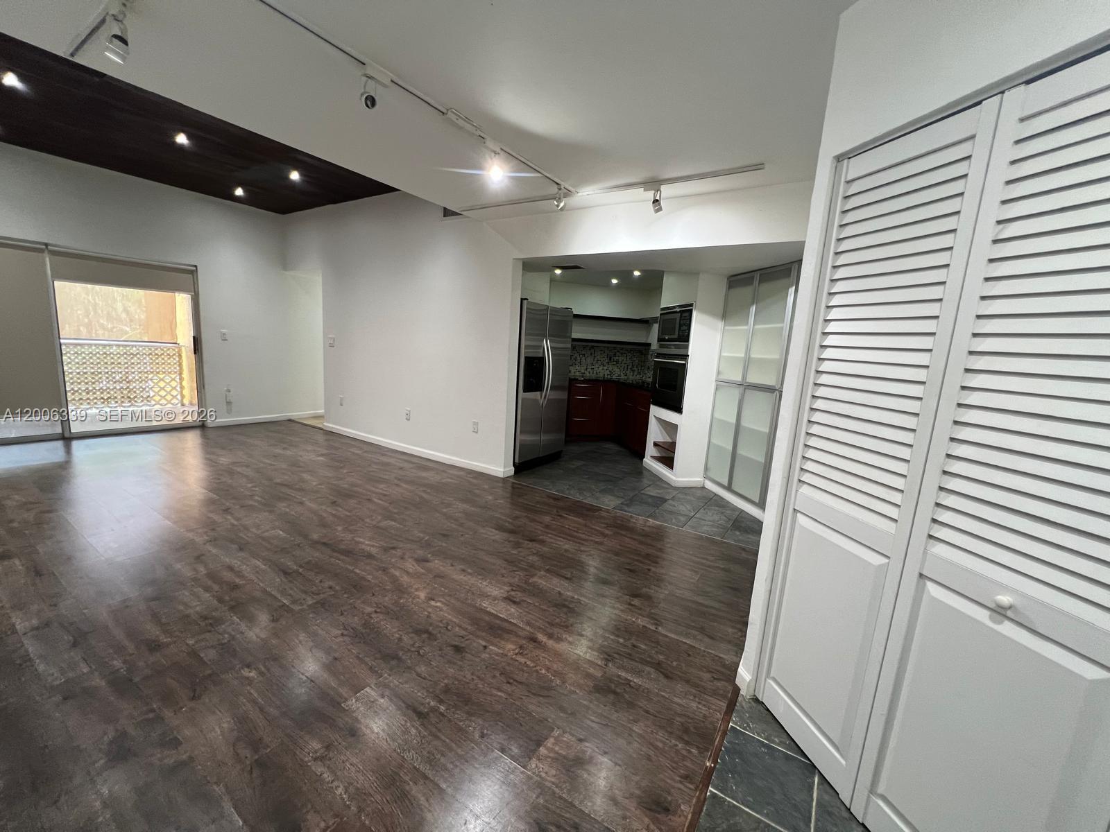 A living area with dark wood flooring leads to a kitchen with stainless steel appliances — 9715 Fontainebleau Blvd # E308, Miami FL 33172, MIAMI, FL
