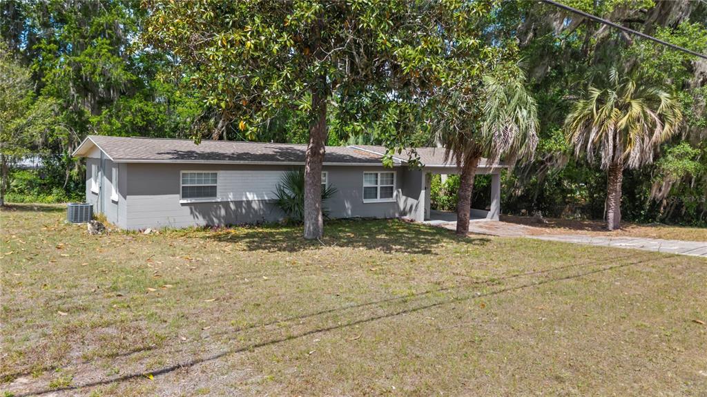 A single-story gray house with a carport sits on a grassy lot with trees — 3918 SE 15TH STREET, GAINESVILLE, FL