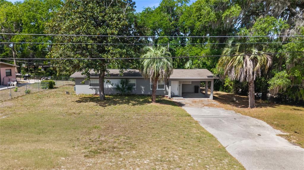 A single-story gray house with a carport sits on a large lot with trees — 3918 SE 15TH STREET, GAINESVILLE, FL
