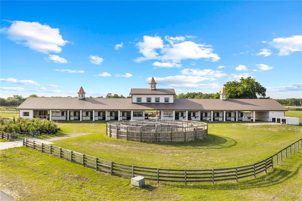 An exterior view of a long horse stable with a central cupola and a round pen — 1345 NE 155TH PLACE, CITRA, FL