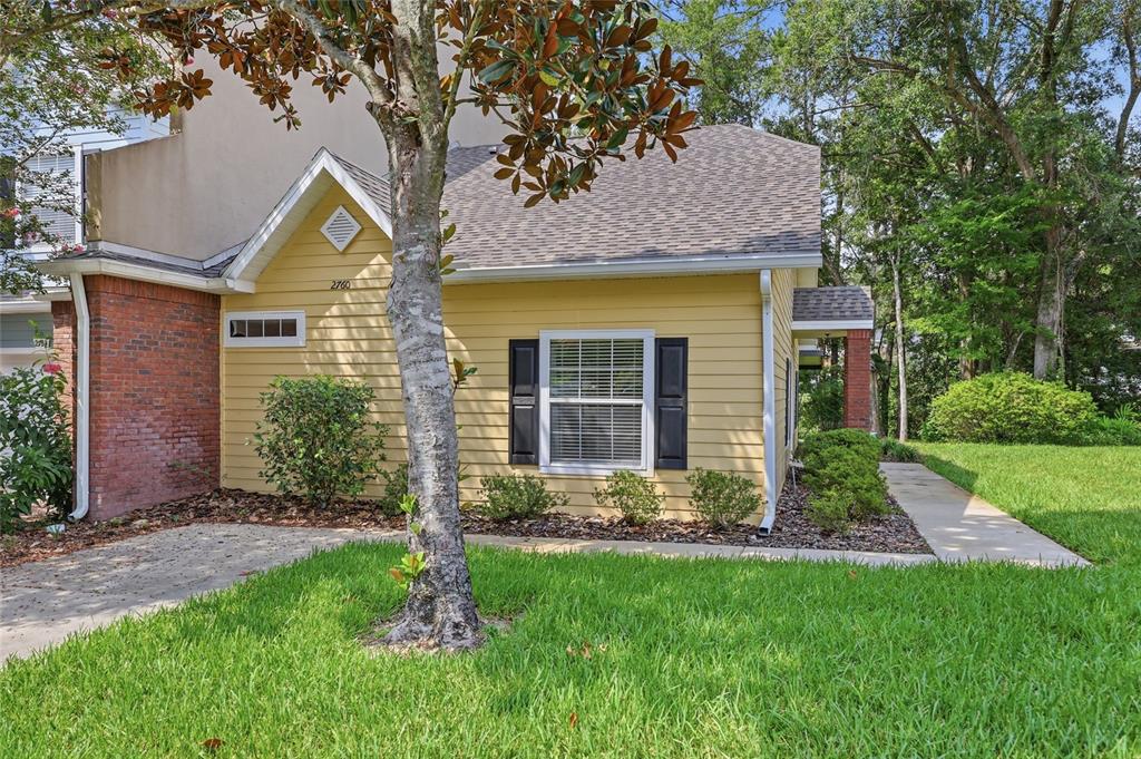 A yellow house with horizontal siding, black shutters, and a brick accent wall — 2760 NW 105TH DRIVE, GAINESVILLE, FL