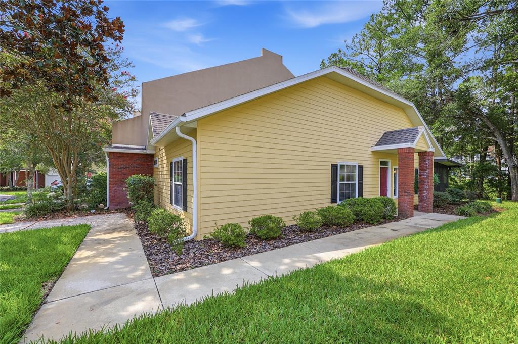 A yellow house with brick accents and a concrete walkway sits on a grassy lawn — 2760 NW 105TH DRIVE, GAINESVILLE, FL