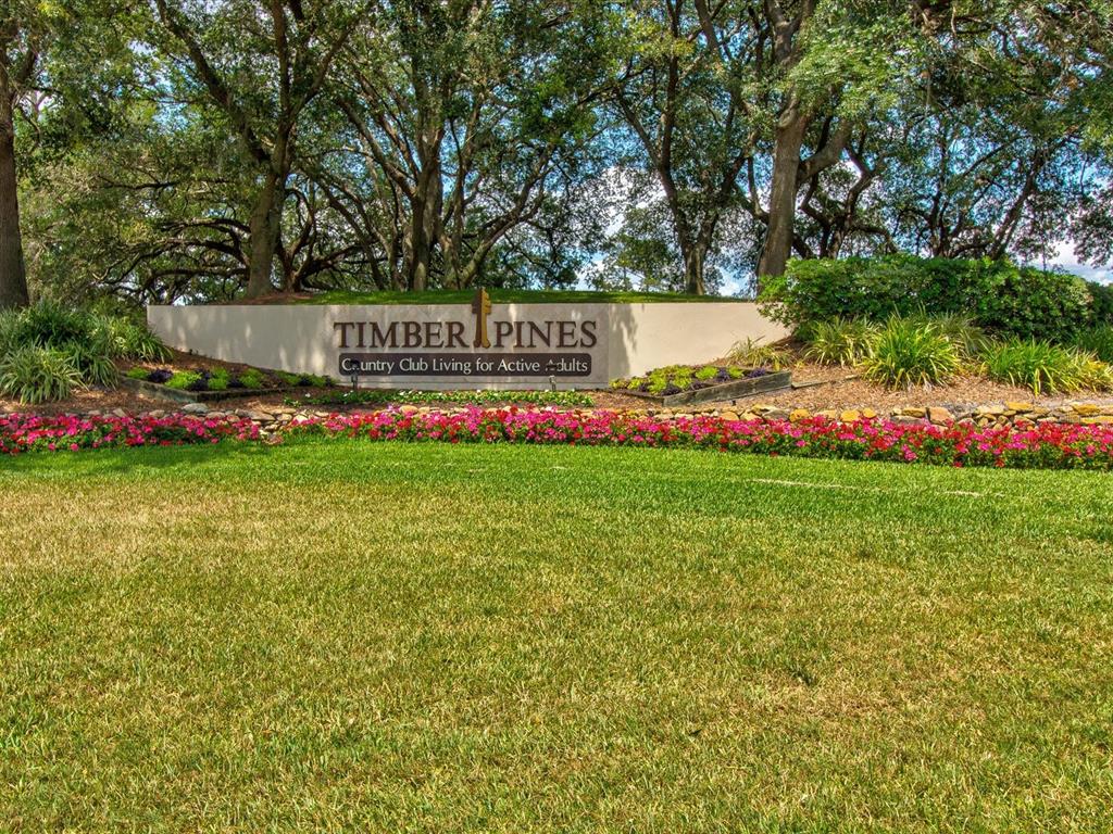 A sign for Timber Pines stands in front of a lawn, flowers, and mature trees — 3123 QUAIL HOLLOW COURT, SPRING HILL, FL