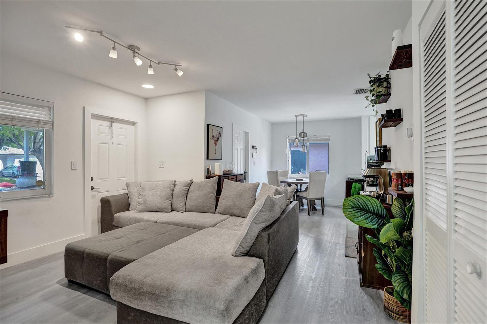 A living room with a gray sectional sofa, light wood-look flooring, and an adjacent dining area — 1590 NW 7th Lane, Pompano Beach FL 33060, POMPANO BEACH, FL