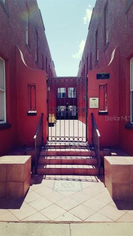 A gated courtyard entrance features red stucco walls, tiled steps, and a metal security gate — 111 S NEWPORT AVENUE UNIT 6, TAMPA, FL