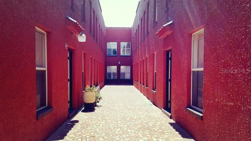 A narrow courtyard with a paved walkway sits between two red stucco apartment buildings — 111 S NEWPORT AVENUE UNIT 6, TAMPA, FL