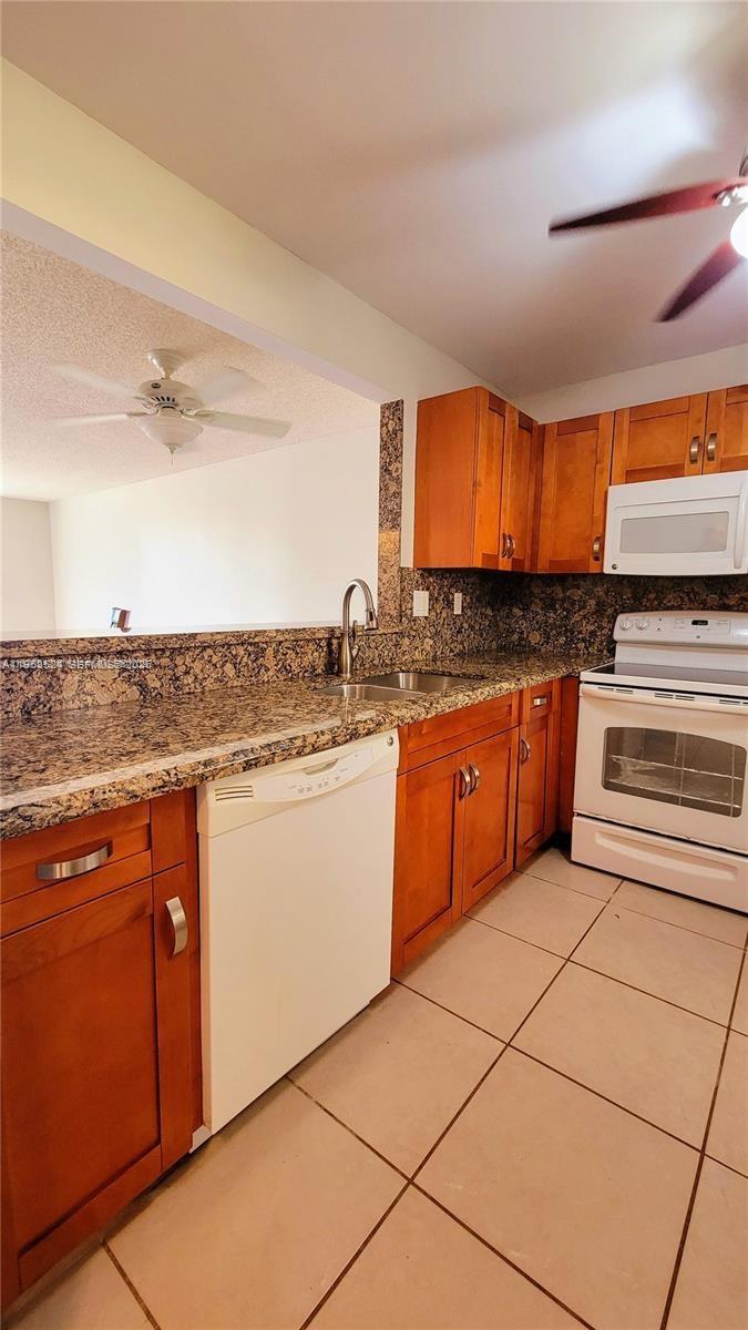 A kitchen features wood cabinets, granite countertops, white appliances, and a pass-through window — 406 NW 68th Ave # 304, Plantation FL 33317, PLANTATION, FL